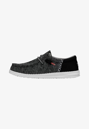 Zapatillas slip-on tejidas en negro y gris con una suela de goma blanca, que presentan una superficie texturizada y un acento negro contrastante en el talón.