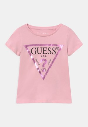 Jasnoróżowy t-shirt z krótkim rękawem z metalicznym różowym logo w kształcie trójkąta oraz czarnym tekstem "GUESS U.S.A." i "WASHED JEANS" z przodu.