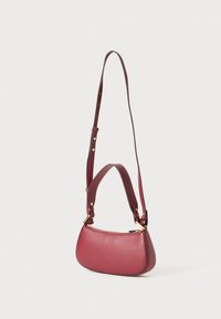 Sac à main en cuir bordeaux avec une forme arrondie, doté d'une fermeture éclair, d'une bandoulière ajustable et d'accents en métal doré.