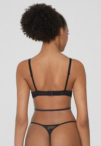 Conjunto de lencería negra con una espalda de encaje transparente, tirantes delgados ajustables, cierre de gancho y ojo, y elementos de diseño minimalistas.