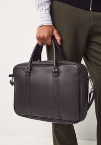 Dunkelbraune Leder-Aktentasche mit glatter Textur, zwei oberen Griffen, Reißverschluss und abnehmbarem Schulterriemen. Mit vertikalen Akzentlinien.