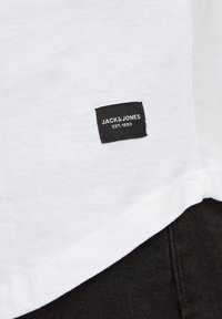 T-shirt in cotone bianco con etichetta rettangolare nera riportante il testo "JACK & JONES" e "EST. 1990" in lettere bianche.