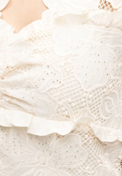 Λευκό δαντελένιο ύφασμα με floral σχέδια, λεπτομέρειες από δίχτυ, μικρές ασημένιες χάντρες και βολάν σε ανοιχτό φόντο.