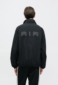 Μαύρο αδιάβροχο μπουφάν με κεντημένο λογότυπο "AIR" στην πλάτη, ελαστική ραφή στο τελείωμα και λεπτομέρειες με αντίθετη ραφή.