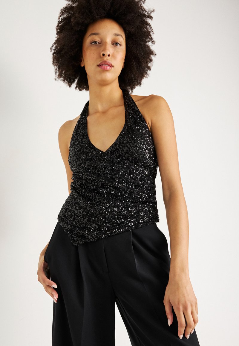 Top halter preto com lantejoulas, decote em V, design ajustado e cintura franzida. Combinado com calças pretas de cintura alta para uma silhueta elegante.