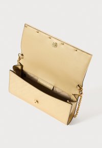 Χρυσή δερμάτινη τσάντα χειρός με κομψό σχέδιο, διαθέτοντας μαγνητικό κλείσιμο, αλυσίδα ώμου και διακριτό ανάγλυφο λογότυπο στο εσωτερικό.