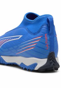 Scarpa sportiva blu con una tomaia testurizzata, caratterizzata da accenti bianchi e rossi. La suola presenta un motivo di trazione nero e una linguetta sul tallone.