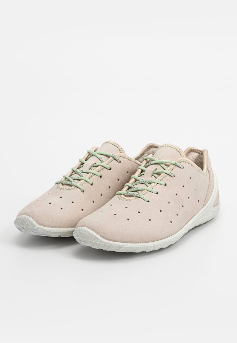 Jasne beżowe buty z perforowanym wzorem, zielonymi sznurowadłami i teksturowaną białą gumową podeszwą. Minimalistyczny i niskoprofilowy kształt.
