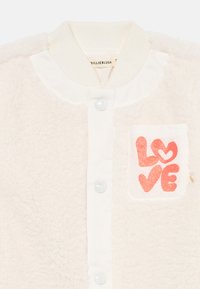 Hvit fleecejakke med ribbestrikket krage, to glinsende knapper og en glitrende rosa "LOVE" grafikk på brystlommen. Myk tekstur.