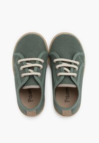 Scarpe in tela di un verde tenue con lacci crema, punta rotonda e suola in gomma beige texturizzata. L'interno presenta il nome del marchio "Pisamon."
