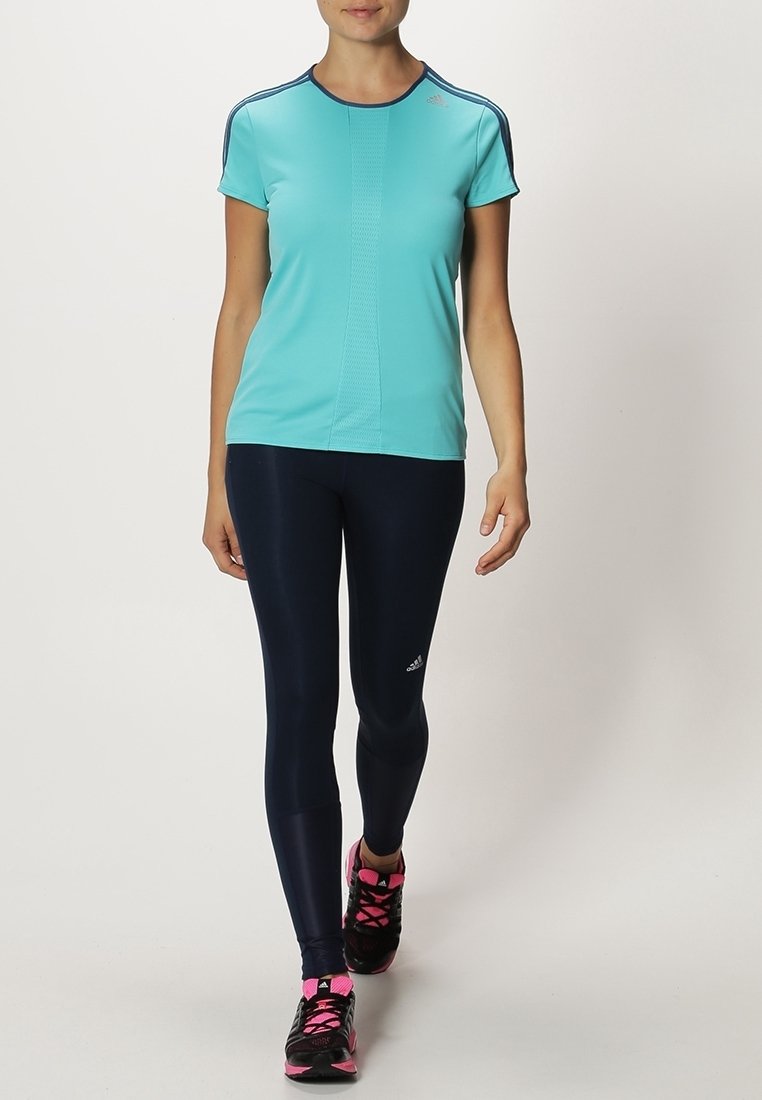 Lichtblauw sportt-shirt met korte mouwen en marineblauwe accenten, gecombineerd met marineblauwe leggings en zwarte sneakers met roze details.