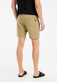 Olijfgroene katoenen shorts met een achterzak, een zachte textuur en gestikte naden, gedragen met zwarte instappers.