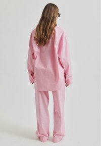 Set di camicia e pantaloni oversize rosa realizzato in tessuto leggero, con vestibilità rilassata e maniche lunghe, dotato di dettagli con bottoni sulla camicia.