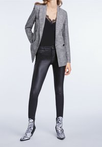 Blazer a quadri grigi sopra un top in pizzo nero, abbinato a pantaloni in finta pelle nera e stivaletti alla caviglia in stampa serpente bianco e nero.