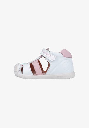 Sandalia blanca y rosa con lados abiertos, correa ajustable, suela de goma y una sutil marca; presenta cortes y una plantilla acolchada.