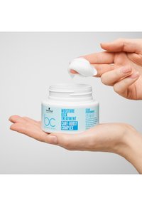 Pot circulaire blanc avec une étiquette bleue indiquant "Moisture Kick Treatment Care-Boost Complex". Produit crémeux blanc sur les doigts. Taille 200 ml.