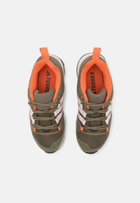 Zelené sportovní boty s oranžovými akcenty, síťovina na svršku, bílé pruhy a texturovaná podrážka. Obsahují šněrování a poutko na patě.