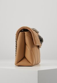 Sac à main en cuir matelassé de couleur beige clair avec une anse en chaîne et une fermeture à pression. Présente des bords arrondis et une légère brillance pour la texture.