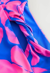 Peldkostīms zilo un rozā audumu ar ziedu rakstu, ar savītu dizaina detaļu. Materiāls šķiet gluds un izstiepjams.