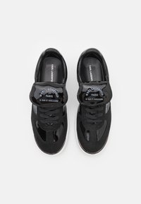 Svarte sneakers med en kombinasjon av semsket skinn og patentmateriale, med en polstret tungemål, snøring og merkedetaljer på stroppen.