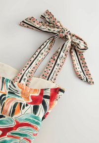 Vestito colorato con motivo a fantasia, con spalline annodate a fiori e scritte su sfondo bianco uniforme.