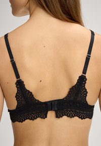 Schwarzes Spitzen-Bralette mit gewellten Rändern, verstellbaren Trägern und Haken-Ösen-Verschluss. Strukturiertes Stoff mit filigranen Spitzenmustern.