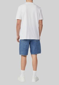 Weißes Baumwoll-T-Shirt und blaue Denim-Shorts. Reflektierende Details an den Shorts, abgeschnittene Säume und weiße Sneakers mit hellen Crew-Socken.