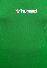 Grünes Sporttrikot aus geripptem Material mit einem figurbetonten Design. Verfügt über ein weißes "hummel"-Logo auf der oberen linken Seite.