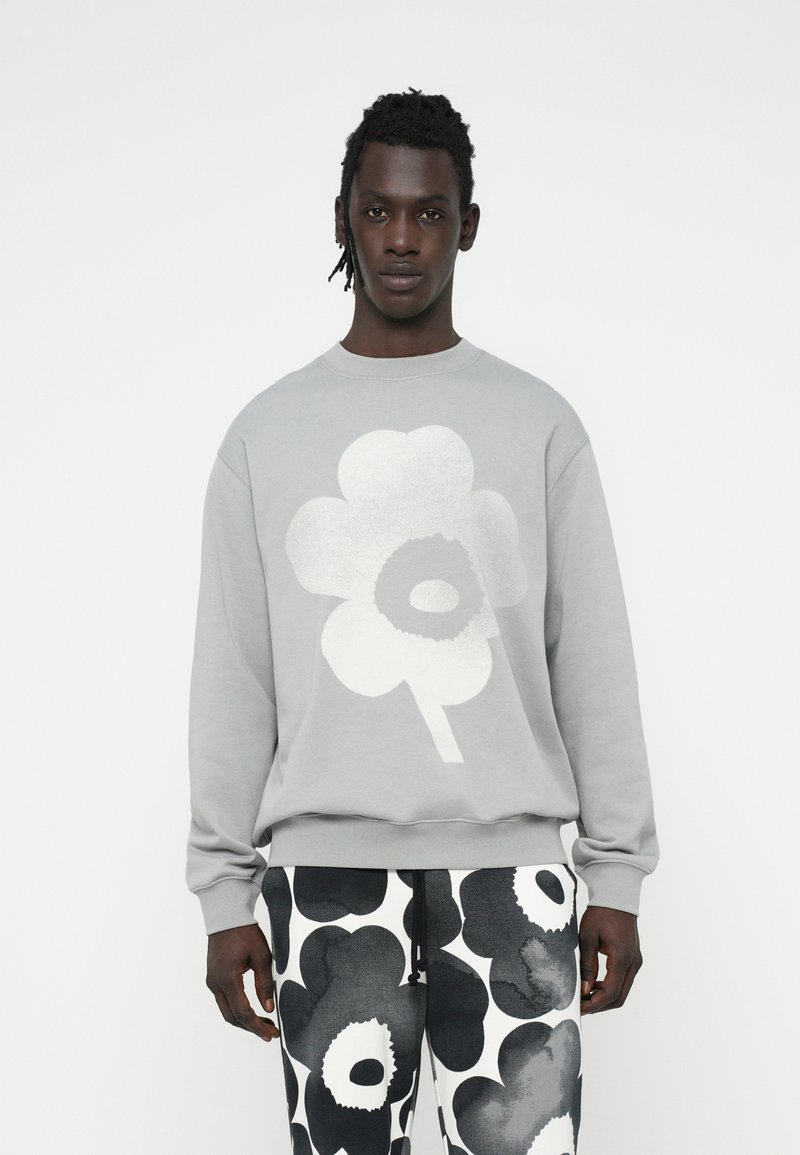 Sudadera gris con un gran gráfico floral blanco en el frente, combinada con pantalones de patrón blanco y negro con atrevidos diseños de flores.