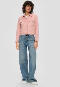 Rosa kurz geschnittene Jacke mit zwei vorderen Taschen, Knopfverschluss und langen Ärmeln, kombiniert mit hellblauen weit geschnittenen Jeans und weißen Turnschuhen.