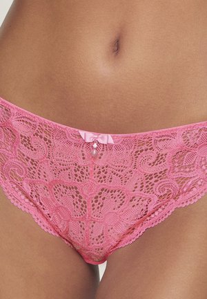 Pink lace bikini underwear with floral patterns and a small satin bow with a pearl charm at the center front on a person’s hips.