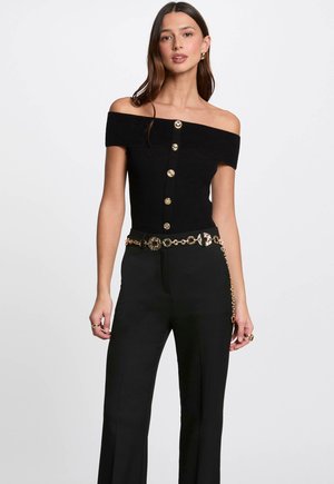 Black off-the-shoulder ribbed top with front gold button detailing, paired with high-waisted black pants and a gold-chain accent belt.
