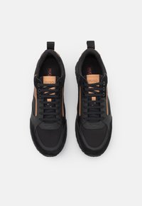 Černé sneakers s hnědými koženými detaily, strukturovanou textilií, polstrovaným jazykem, kulatými tkaničkami a gumovou podrážkou; logo viditelné na jazyku.