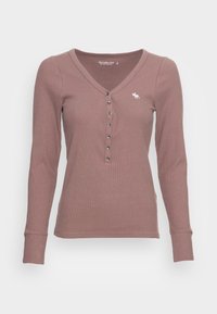 Mauve geripptes Langarm-Henley-Shirt mit V-Ausschnitt, sieben Knöpfen und kleinem weißen Elch-Logo auf der linken Brust.