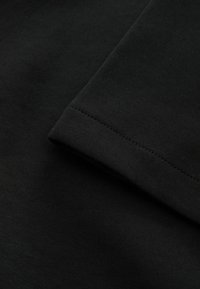 Zwarte katoenen stof met een gladde textuur, met een opgevouwen mouw die een naadloze zoom en consistente steekdetails toont.