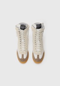 Sneaker alte in pelle beige e bianca con dettagli in camoscio. Presentano un design con lacci e una suola in gomma con finitura testurizzata.