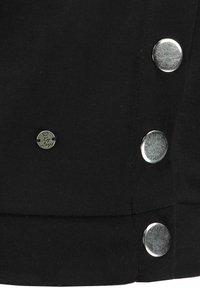 Tela negra con una textura suave, que presenta cuatro broches de metal plateado y una pequeña etiqueta de logotipo plateada, ubicada en una costura.