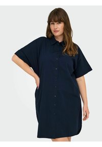 Rochie cămașă bleu marin cu mâneci scurte, cu deschidere cu nasturi în față, croi lejer și buzunare laterale. Material moale cu o textură netedă.
