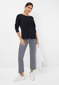 Marineblauwe lange mouw top met een bootcol, gecombineerd met gestreepte cropbroeken in blauw en wit. Witte sneakers maken de outfit compleet.