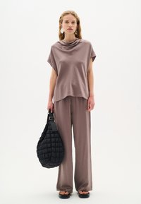 Top leggero marrone chiaro, ampio e drappeggiato, con maniche a cappuccio e pantaloni abbinati a gamba larga. Tiene una borsa nera testurizzata con tracolla.