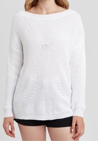 Biała sweter wykonany na drutach o luźnym kroju, z szerokim dekoltem, wzorami teksturowymi oraz ściągaczami przy mankietach i dolnej części. Widoczne krótkie rękawy.