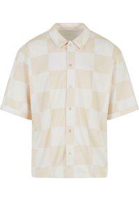 Chemise à manches courtes à boutons beige clair avec un grand motif à carreaux. Dotée d'un col classique et de boutons sur le devant. Texture de tissu lisse.