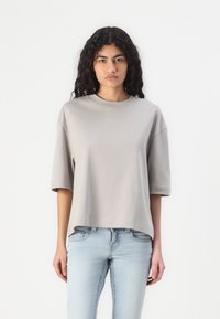 Lys grå oversized t-skjorte med rund hals og korte ermer, laget av myk stoff, paret med lyseblå jeans.