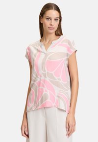 Bluzka z krótkim rękawem z lekkiego materiału, z różowym kwiatowym wzorem na beżowym tle, z dekoltem w kształcie litery V i zaokrąglonym dołem.