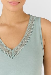 Top sin mangas de color azul claro con un borde de encaje en forma de ola a lo largo del escote en V. Tejido suave con un ajuste casual y sin adornos adicionales.