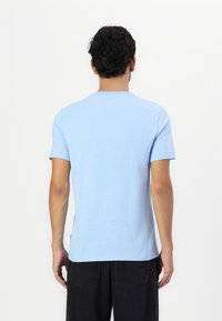 Hele sinine puuvillane T-särk lühikeste varrukatega, ümar kaelus ja sirge lõige, koos mustade teksadega. Sile tekstuur, nähtavaid mustreid pole.