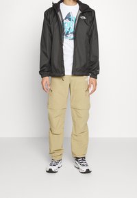 Black lightweight jacket with hood, white graphic t-shirt, beige cargo pants, and black and white sneakers with mesh detailing.