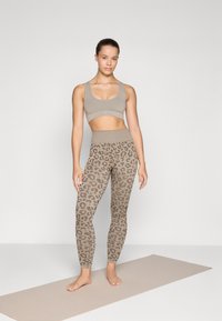 Kaki sports-bh kombinert med matchende leopardmønstrede leggings. Begge laget av myk, elastisk stoff; slankt design med høy midje.