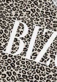 Luipaardprintstof met een beige achtergrond, met grote witte tekst die "BIZ" spelt. Het materiaal lijkt zacht en textuur te hebben.