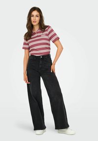 Stribet polo skjorte i nuancer af vinrød med hvide linjer, parret med høj talje og brede sorte jeans samt hvide sneakers.